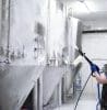 A Worker's Hand Hold A High Pressure Cleaner Gun And Put Foam On Equipment On The Factory