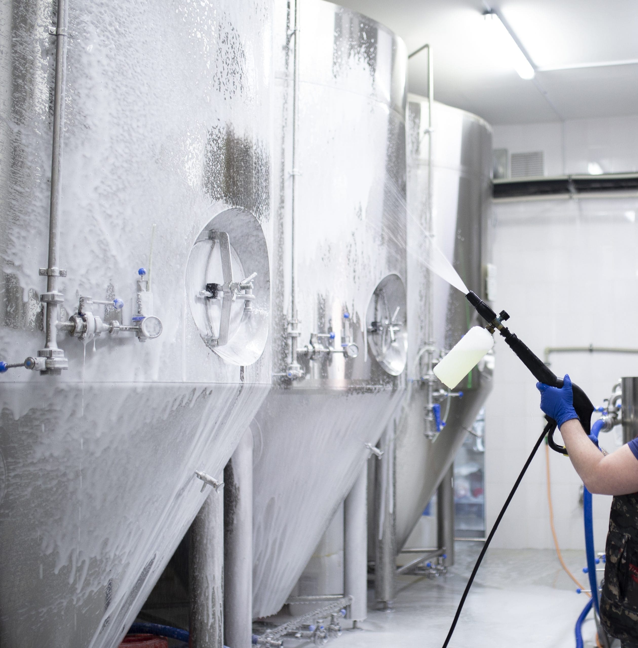 A Worker's Hand Hold A High Pressure Cleaner Gun And Put Foam On Equipment On The Factory