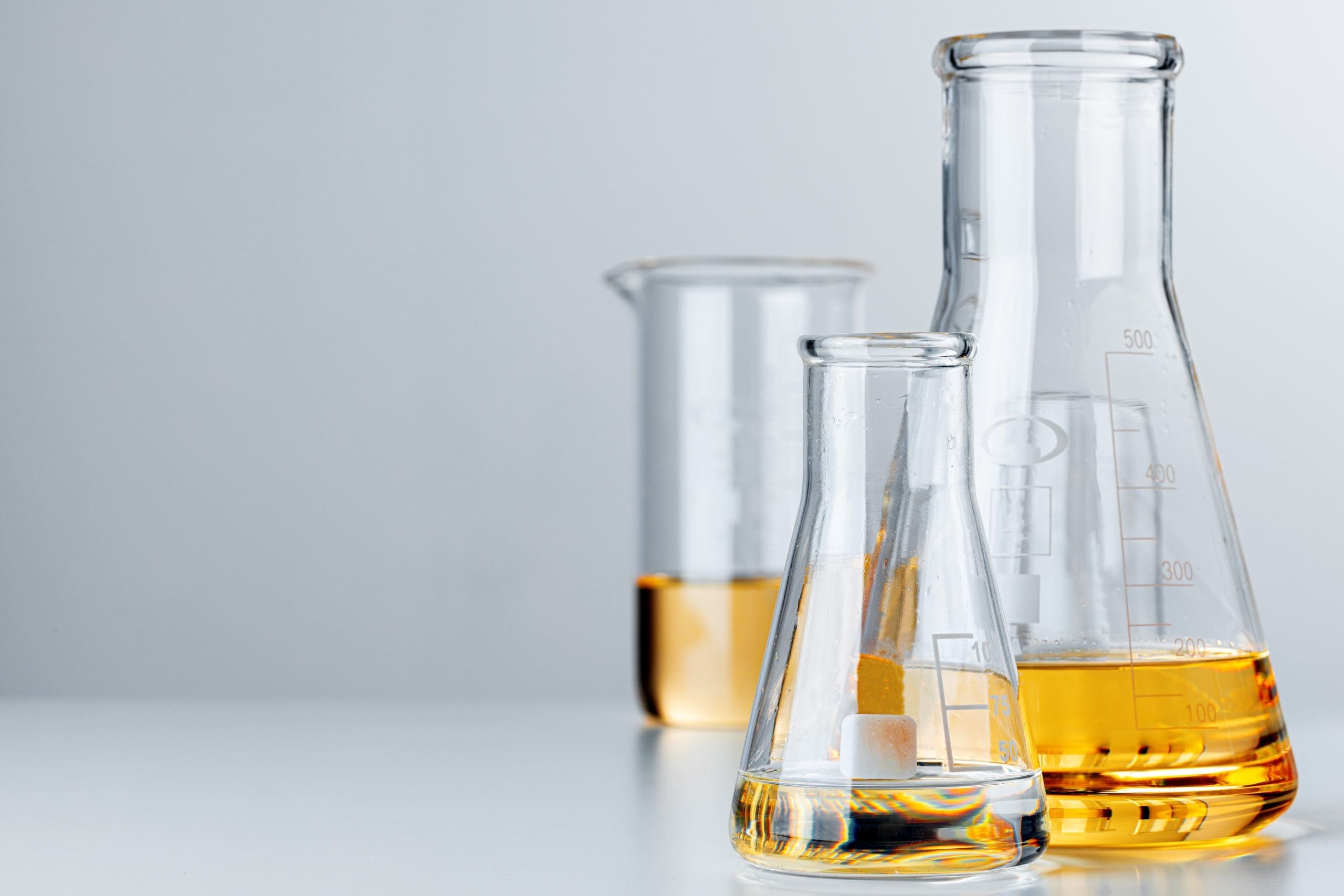 Laboratory Glassware With Yellow Oily Liquid On Grey Background