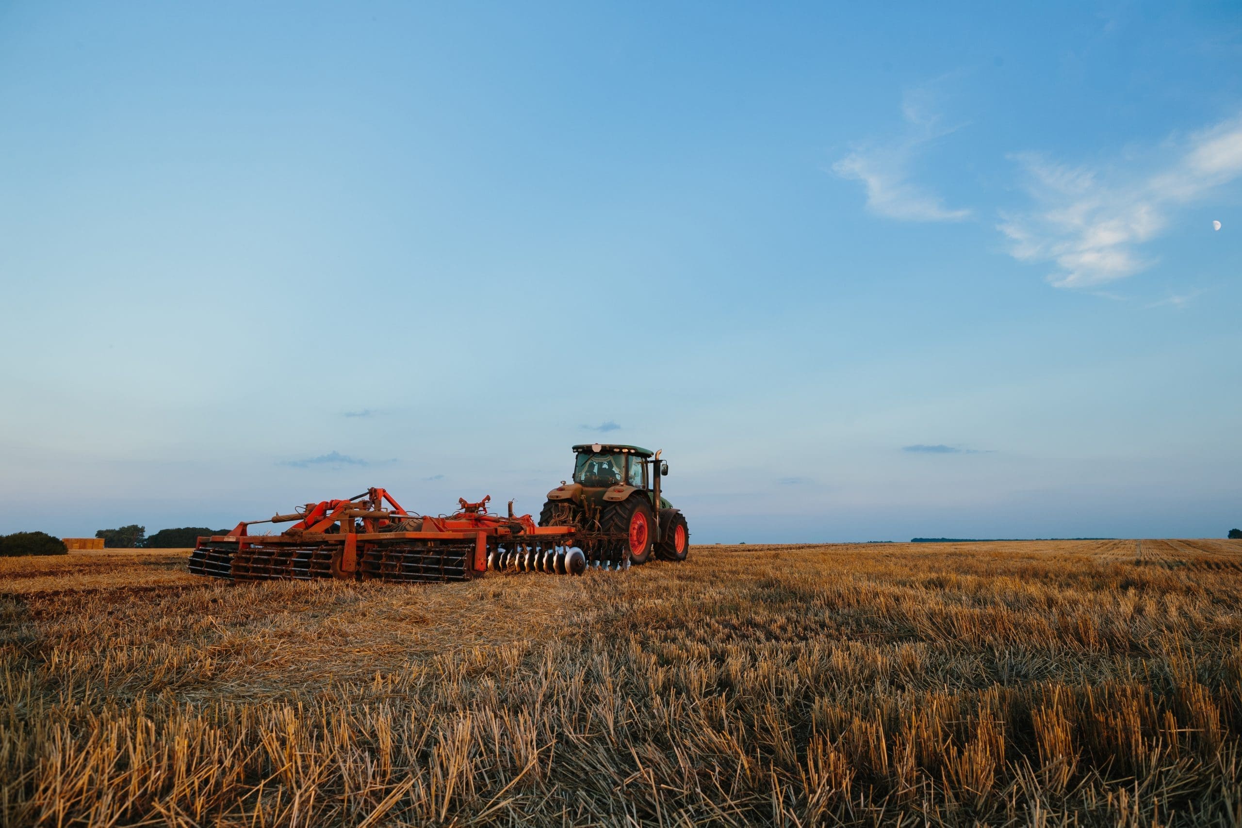 Modern Tractor With A Heavy Trailed Disc Harrow Works A Wide Hilly Field. Autumn Or Spring Agricultural Campaign