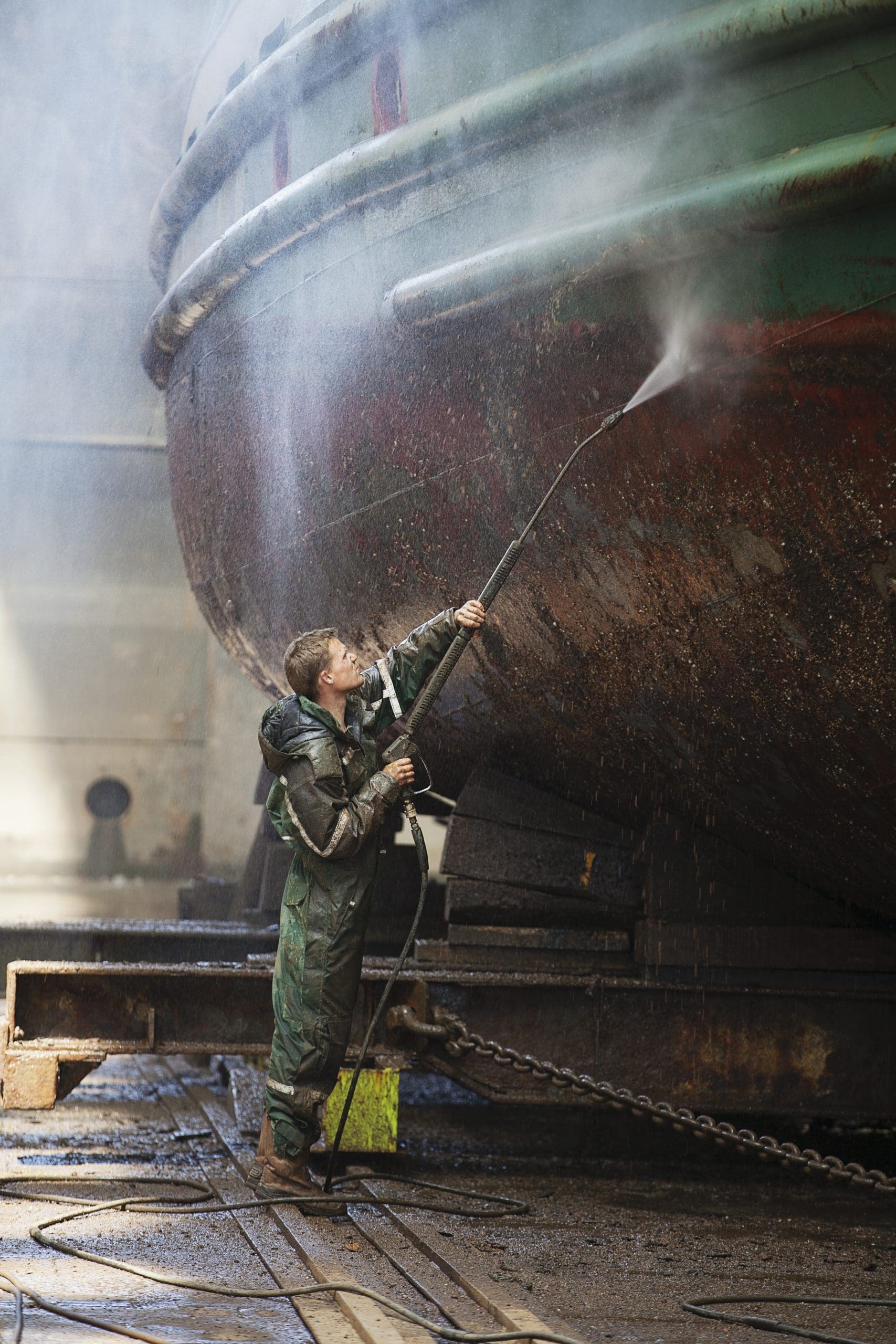 Shipyard Worker Cleaning Boat With High Pressure Hose