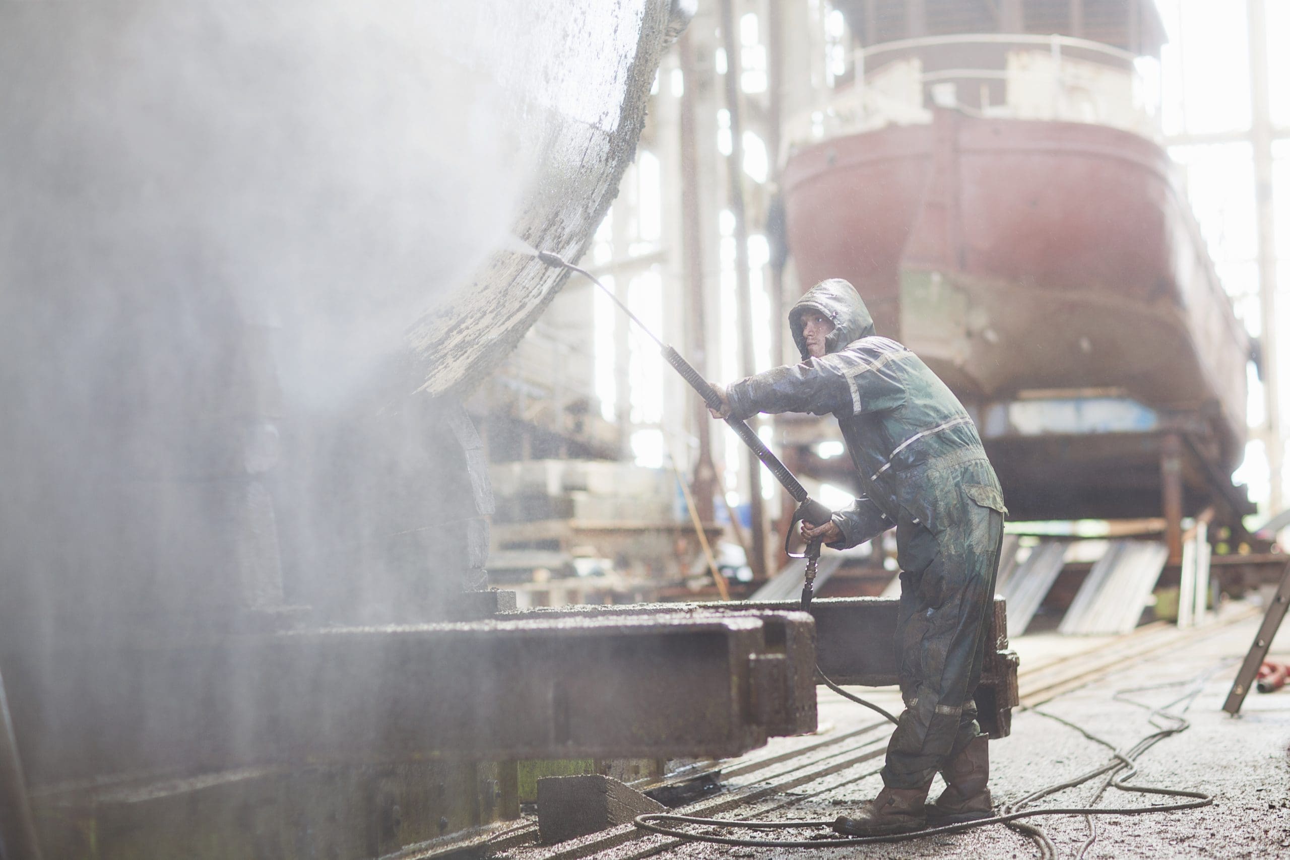 Worker Using High Pressure Hose On Boat In Shipyard Workshop